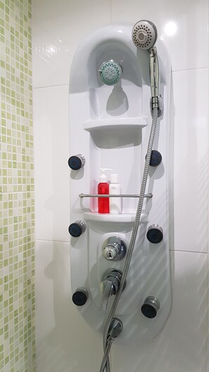 Seinään asennettu suihku, jossa on useita säätimiä, saippua-annostelija ja shampoopullo.