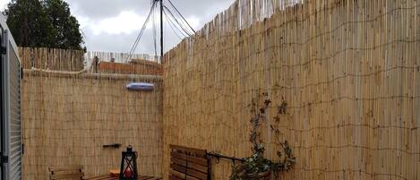 A patio area with a bamboo fence, a table with chairs, and a hanging plant.