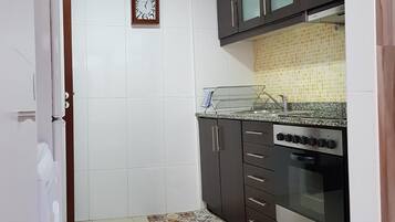 Una cocina compacta con azulejos blancos, armarios oscuros, horno de acero inoxidable y un tapete estampado.