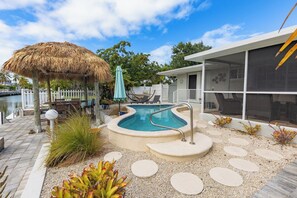 A swimming pool with a thatched roof structure, a covered seating area, and a view of a body of water.