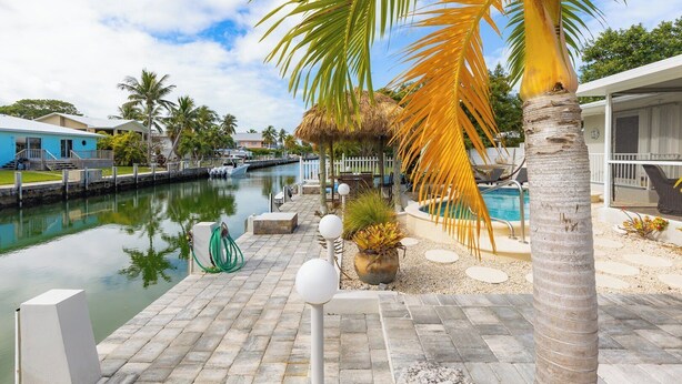A waterfront property with a swimming pool, palm trees, and a dock with boats. - Manatee Oasis 4bed/3bath single family home with private pool & dockage located on the gulf side of Marathon (Marathon)