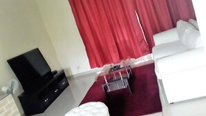 A room with a white sofa, a red curtain, and a flat-screen TV on a stand. - Red Dot Lodge (Randburg)