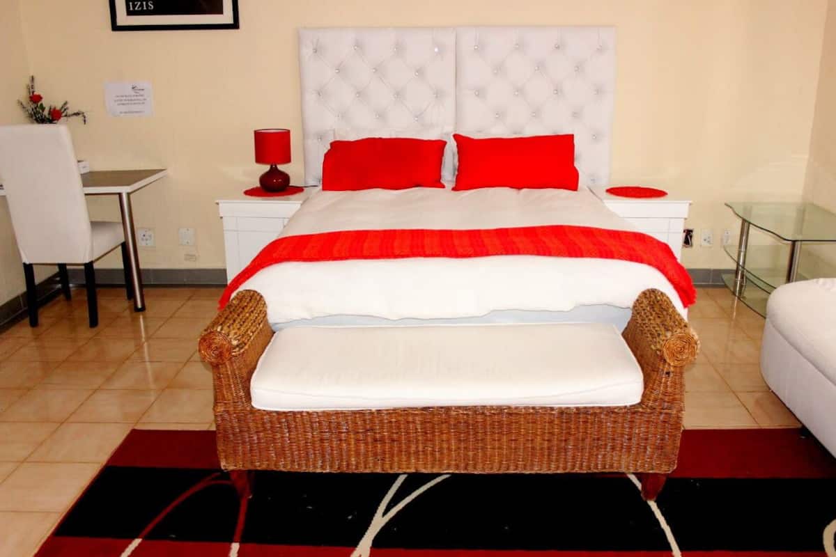 Una habitación de hotel con una cama grande, una silla de mimbre, un escritorio y una mesa de vidrio.