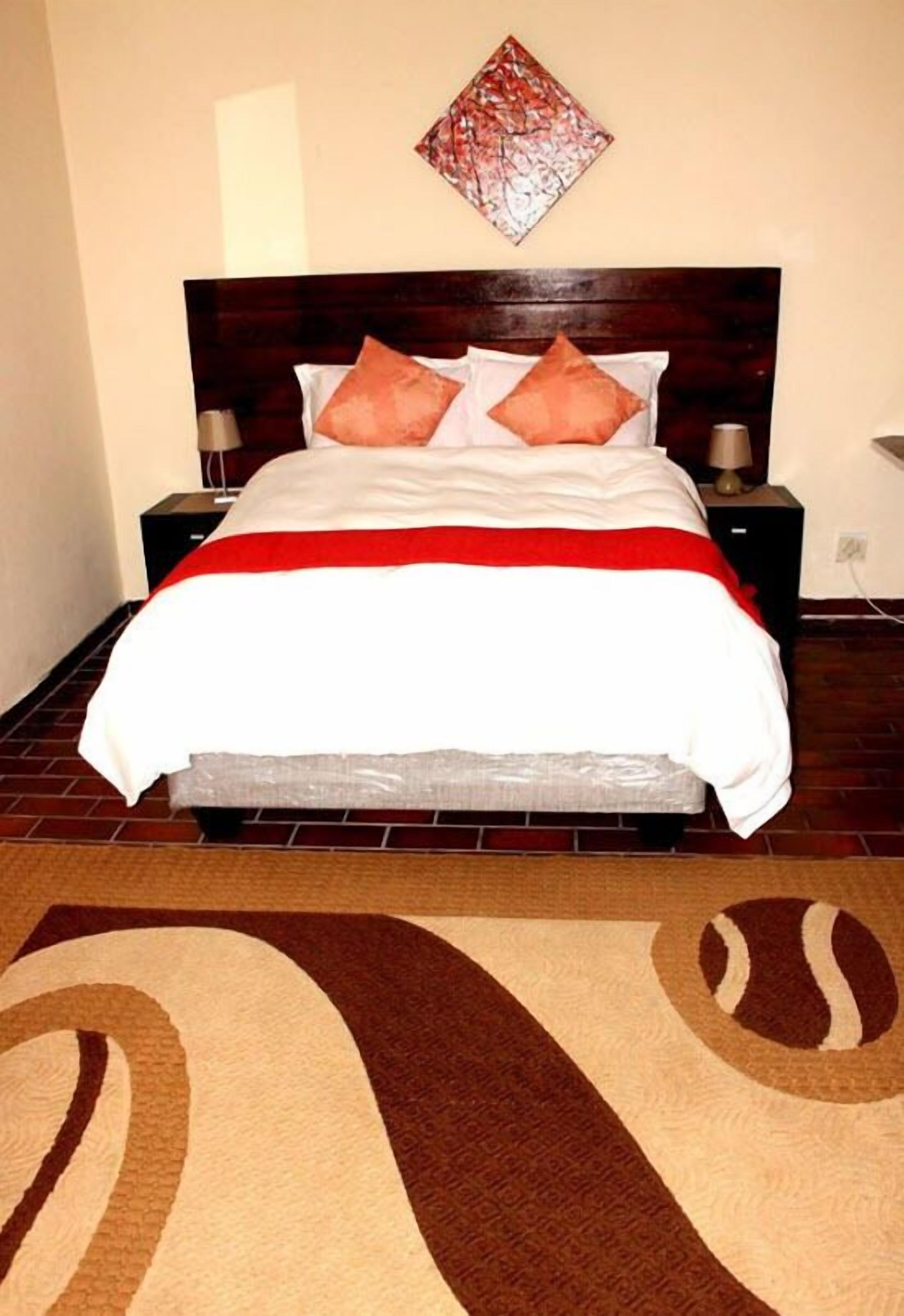 Una cama bien hecha con una colcha blanca y roja, dos almohadas y un cabecero de madera.