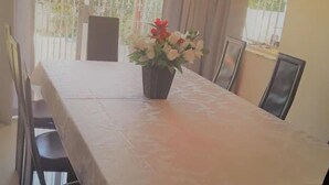 A dining area with a table covered by a white tablecloth, surrounded by chairs. A potted plant with flowers is placed on the table. - Red Dot Lodge (Randburg)
