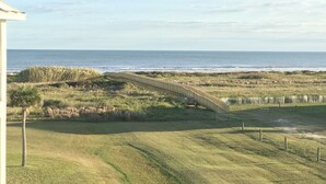 A coastal landscape with a wooden bridge leading to the beach, surrounded by grassy dunes and a clear view of the ocean. - Designer Beach Retreat -Gulf views-Walk2Sand -Family & Dog Friendly (Galveston)