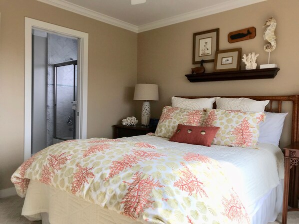 A bedroom with a bed, a nightstand, a lamp, and a door leading to a bathroom.
