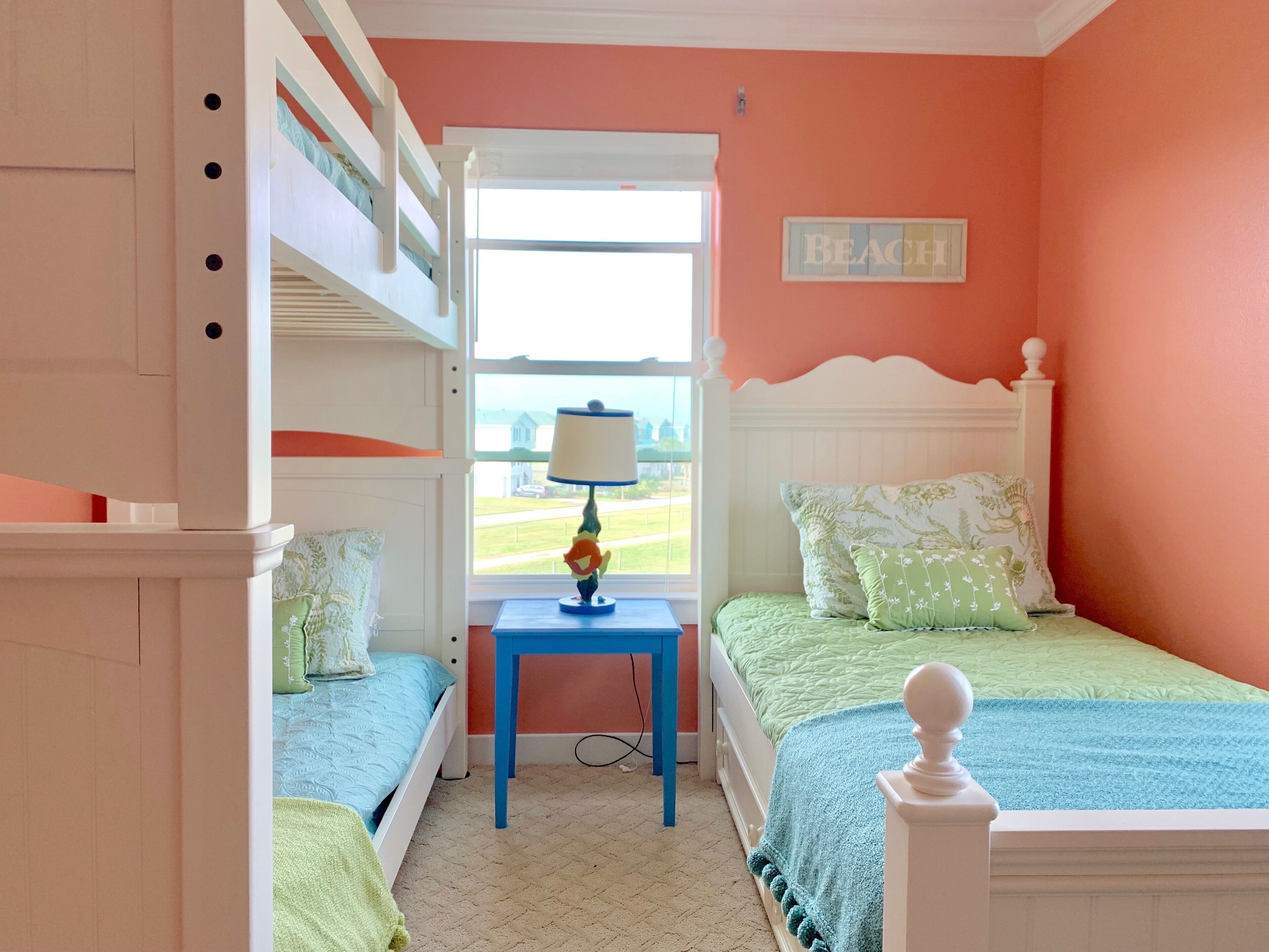 A bedroom with bunk beds, a small table with a lamp, and a view of the outdoors.