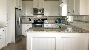 A modern kitchen with white cabinetry, stainless steel appliances, a granite countertop, and a built-in oven. - Designer Beach Retreat -Gulf views-Walk2Sand -Family & Dog Friendly (Galveston)