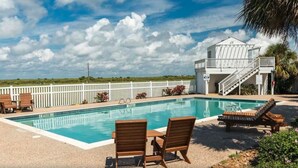 A swimming pool with lounge chairs, a white building with a staircase, and a view of the ocean. - Designer Beach Retreat -Gulf views-Walk2Sand -Family & Dog Friendly (Galveston)