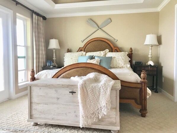 A bedroom with a wooden bed, two bedside tables, a wall-mounted paddleboard, and a large window with curtains.
