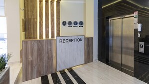 Un espace d’accueil avec un comptoir de réception en bois, une enseigne indiquant « RÉCEPTION », des horloges affichant différents fuseaux horaires et un ascenseur.