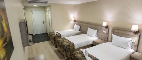 Habitación de hotel con tres camas, un escritorio y una puerta que da a otra habitación.