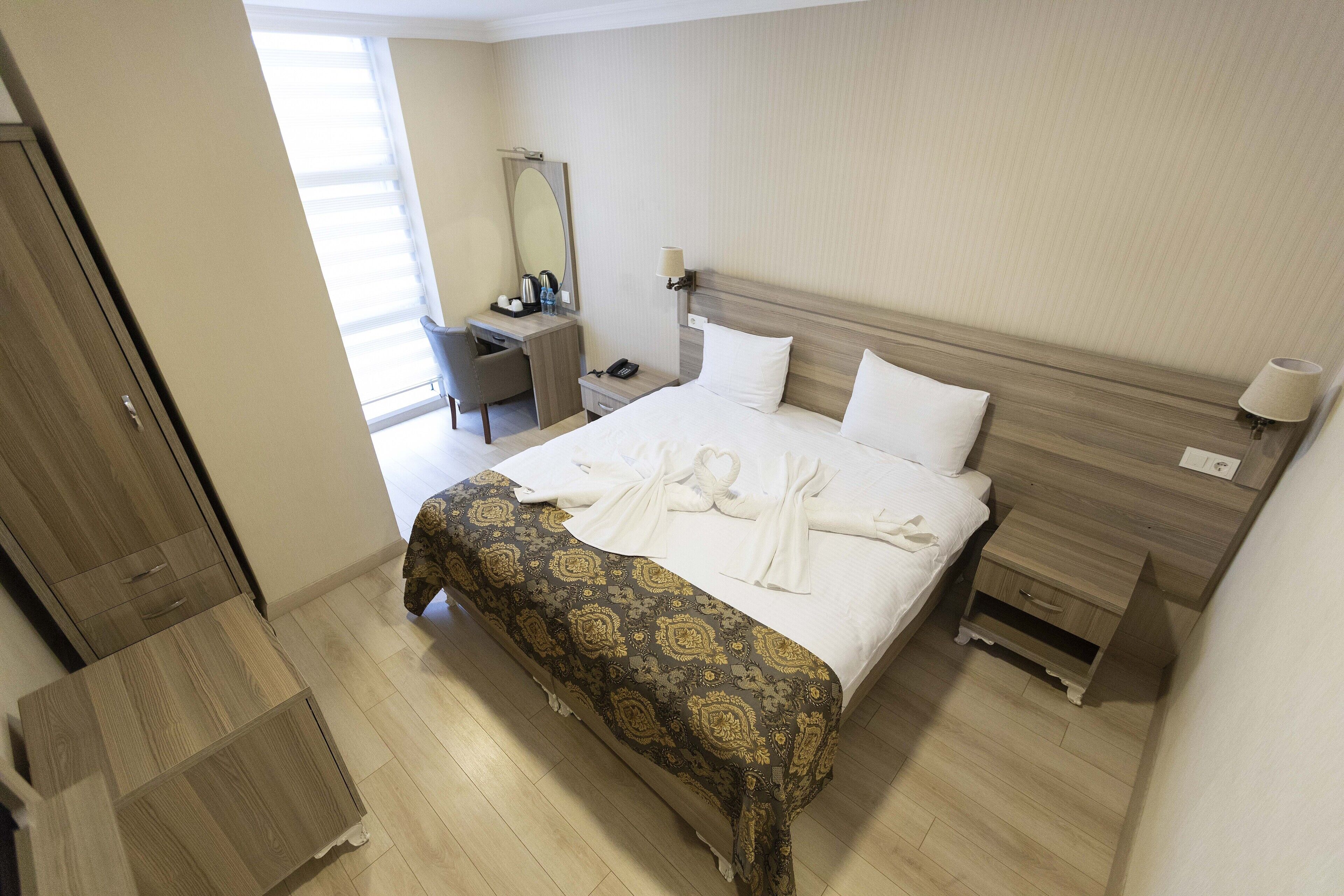 A hotel room with a bed, bedside table, nightstand, desk, chair, and a mirror.