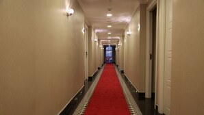 Un couloir d’hôtel avec un tapis rouge, des murs blancs et des carreaux noirs et blancs formant un motif.