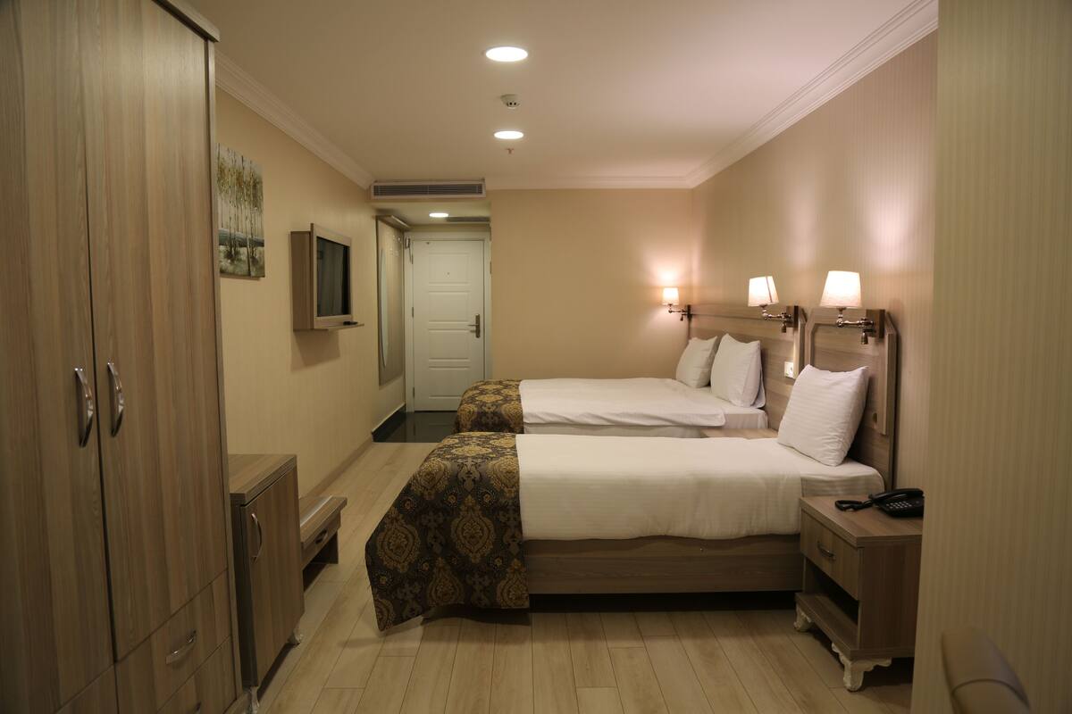 A hotel room with two beds, a wardrobe, a television, bedside lamps, and a telephone.