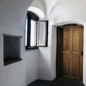 A corner room with a wooden door, a small window with a mirror, and a shelf. - AgroPobitzer (Malles Venosta)