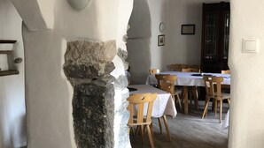 Un intérieur rustique avec des murs en pierre apparentes, des poutres en bois et un coin repas agrémenté de chaises et de tables en bois.