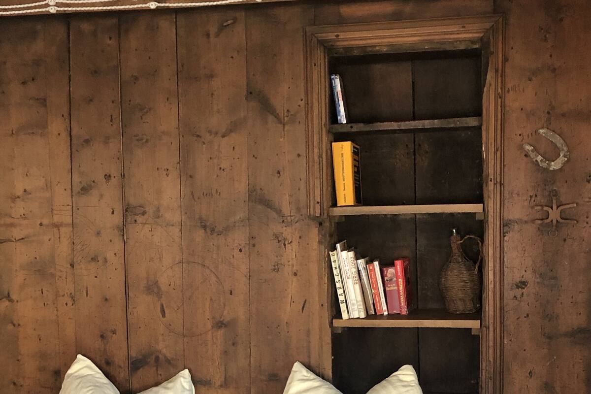 A rustic wooden room with a bookshelf containing books and a decorative item. There are two beds with white bedding and pillows.