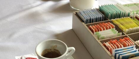 Una mesa con una taza de café, una jarra de leche y una caja de bombones variados.