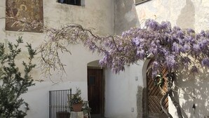 Une cour avec une table et des chaises, une porte en bois et un arbre à fleurs violettes.