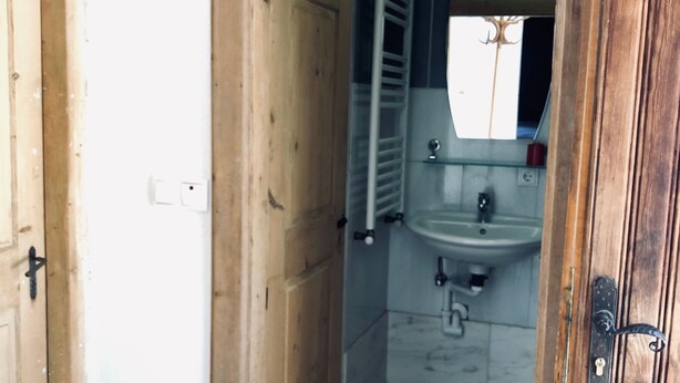 A wooden door leading to a bathroom with a sink, mirror, and towel rack. - AgroPobitzer (Malles Venosta)