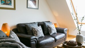 Een moderne woonkamer met een donker leren bank, decoratieve kussens, een geweven bijzettafeltje en een chocoladecake op tafel.