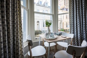 A dining area with a table set for four, a vase with flowers, and a view of the city through large windows. - 2 Sussex Place (Plymouth)