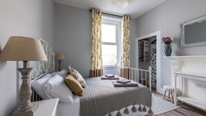 A bedroom with a bed, two bedside lamps, a window with curtains, a fireplace, and a mirror on the wall. - 2 Sussex Place (Plymouth)