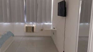 A room with a flat-screen TV mounted on the wall, a small built-in air conditioning unit, and a window with sheer curtains. - Hotel Amazônia Belém (Belém)