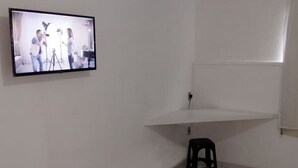 A room with a flat-screen TV mounted on the wall, a black stool, and a white shelf. - Hotel Amazônia Belém (Belém)