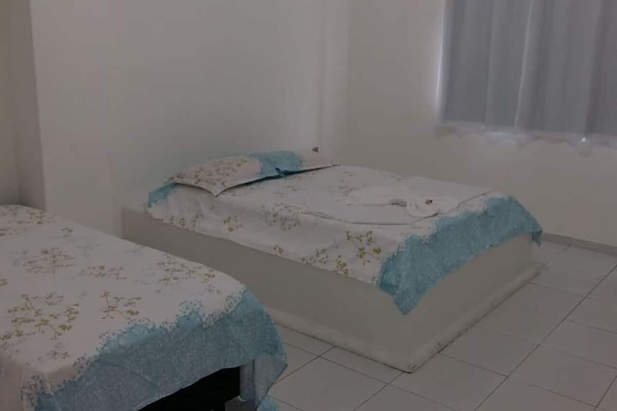 Ein kleines, sauberes Zimmer mit zwei Einzelbetten, weißen Wänden und einem Fliesenboden.