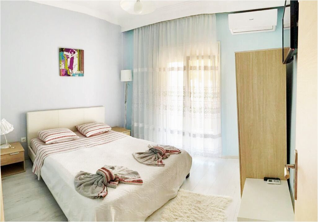 A bedroom with a bed, a bedside table, a lamp, a wardrobe, and a window with curtains.