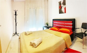 Un dormitorio con una cama, una silla, perchero y ventana con cortinas.