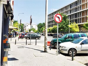 Una calle con coches aparcados, una señal de prohibido girar a la izquierda y un edificio con grandes ventanales.