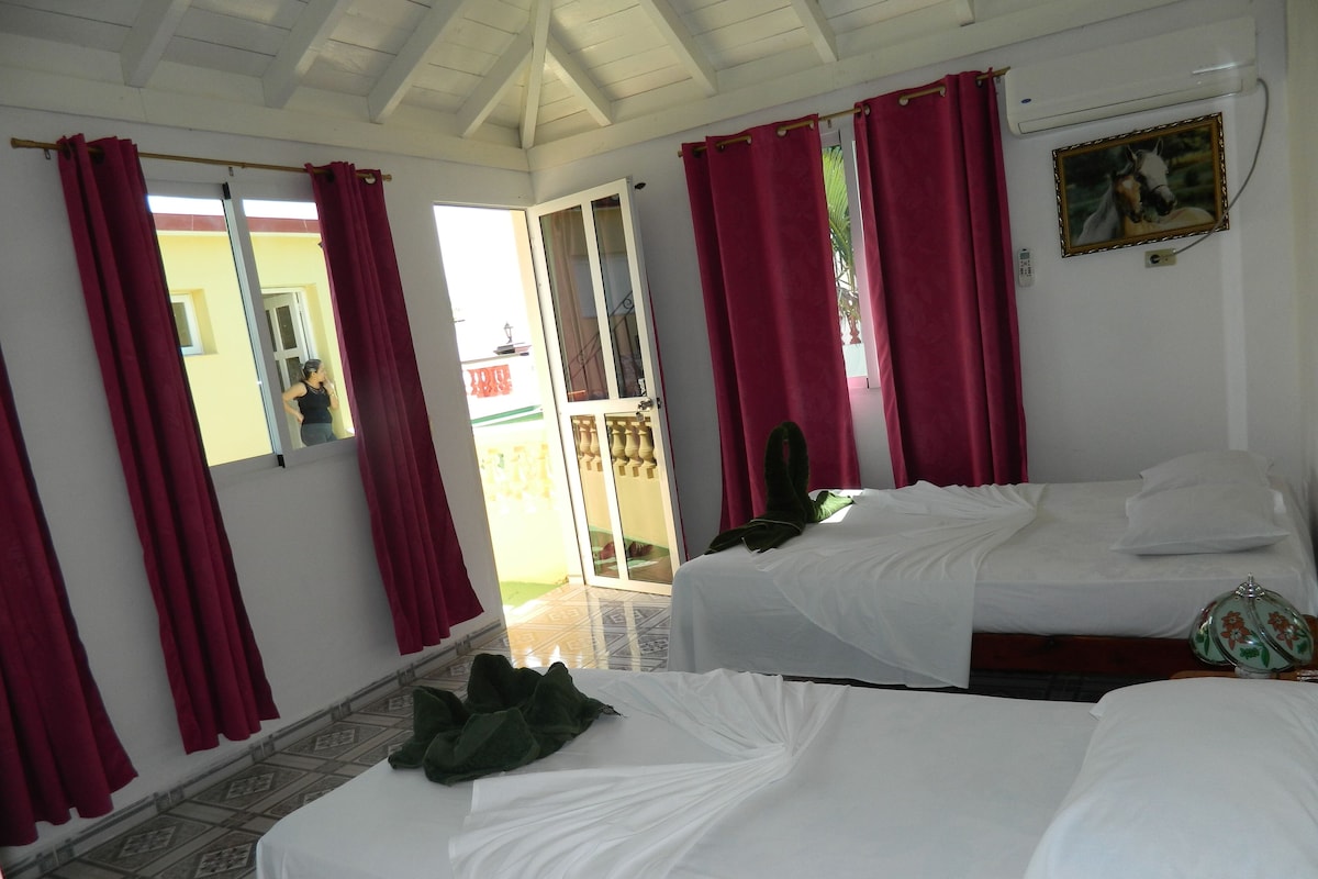 Une chambre d’hôtel avec deux lits, des rideaux rouges, un tableau et un sol carrelé.