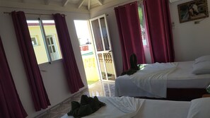 Une chambre d’hôtel avec deux lits, un balcon et des rideaux rouges.