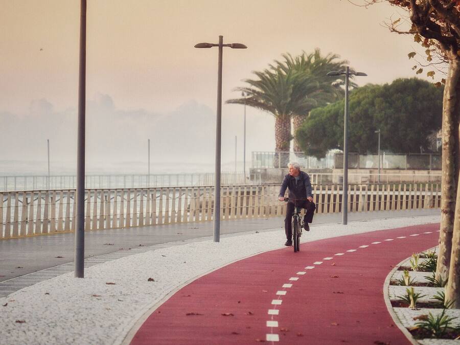 A person riding a bicycle on a red pathway beside a waterfront.