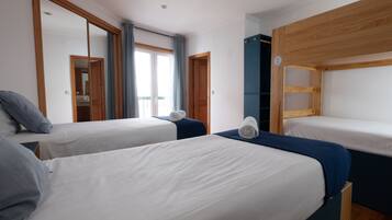 A hotel room with two single beds, a wooden wardrobe, a mirror, and a window with curtains.