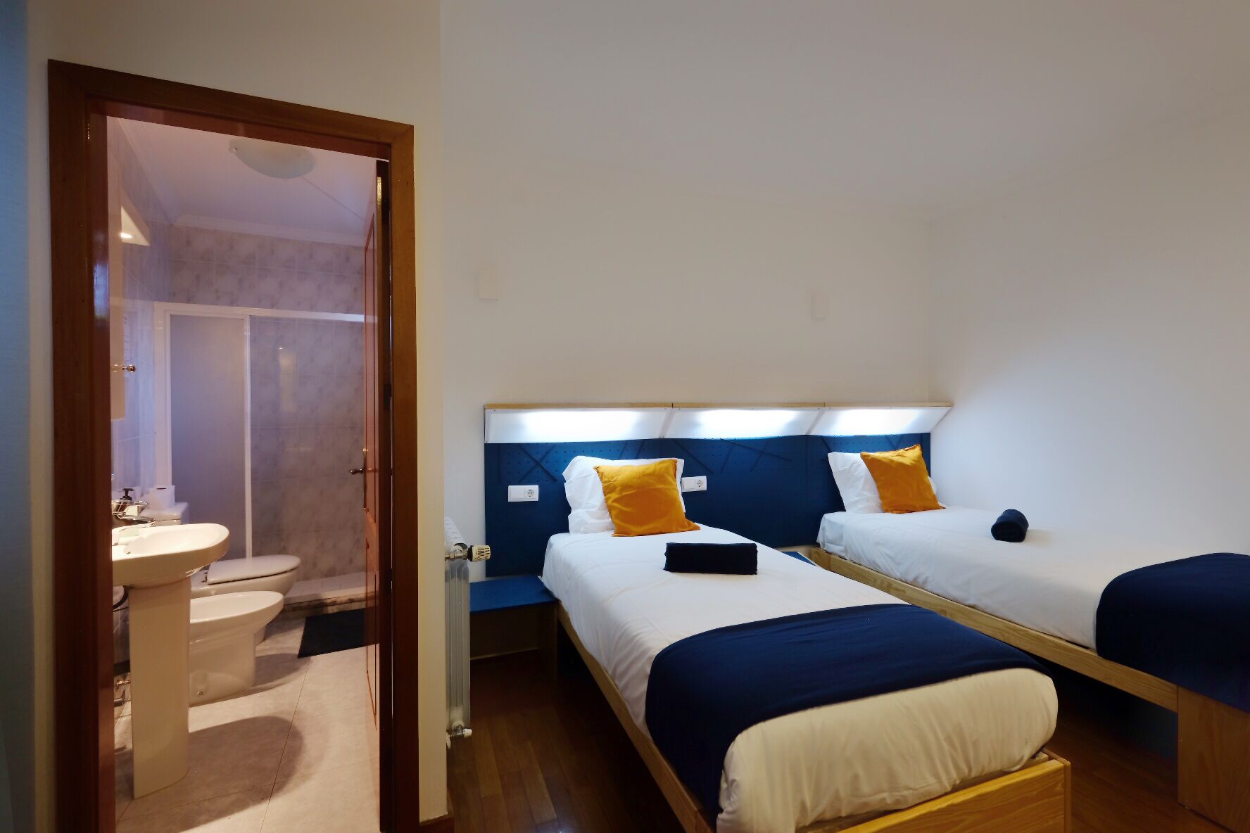 Una habitación con dos camas, un baño con inodoro y lavabo, y suelo de madera.