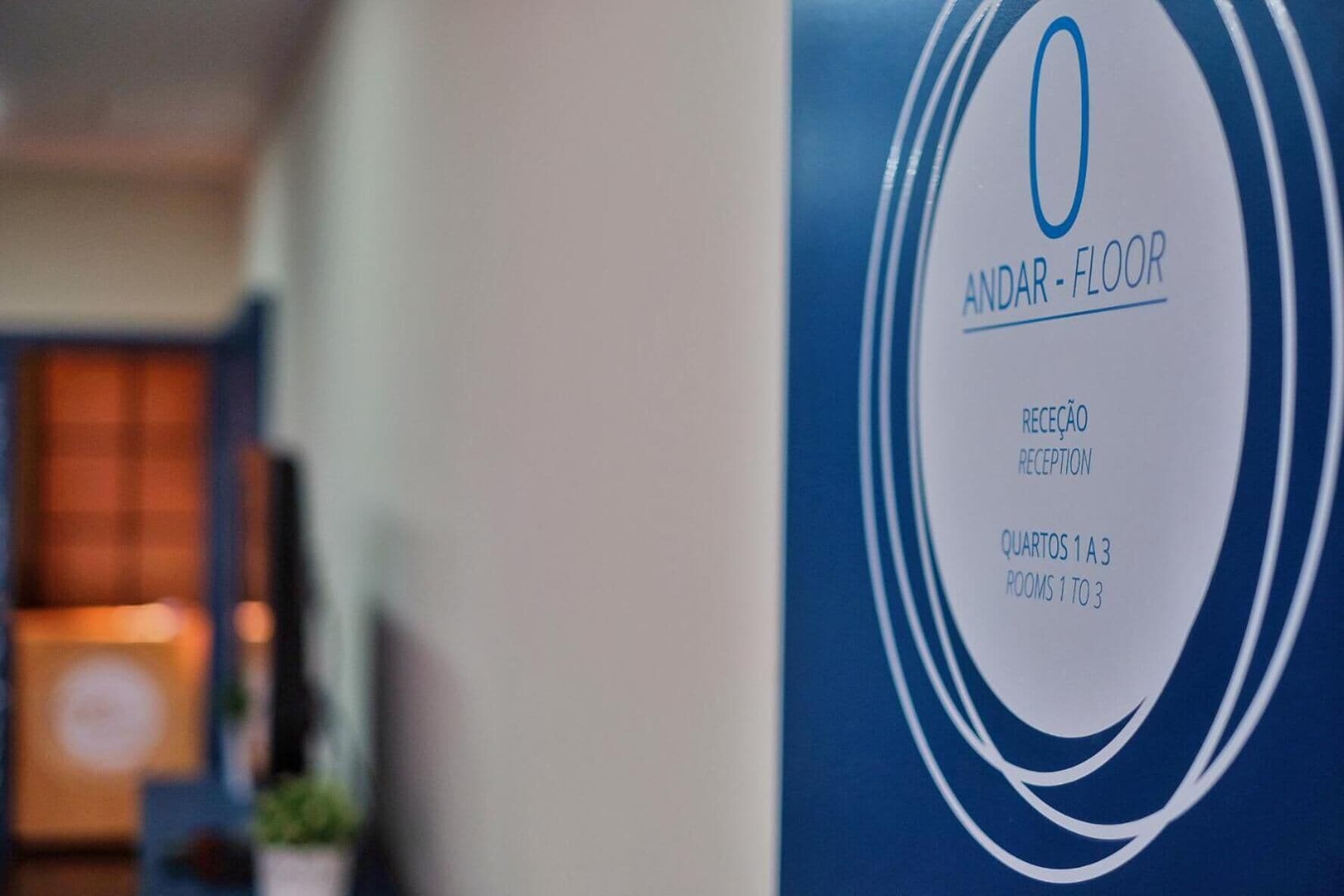 A reception desk with a sign indicating 'ANDAR - FLOOR' and 'RECEPTION' along with 'QUARTOS 1 A 3' suggesting rooms 1 to 3 are available.