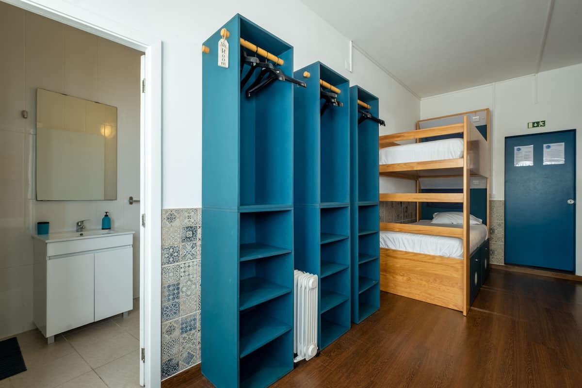 A dormitory room with bunk beds, a white sink, and a blue door.