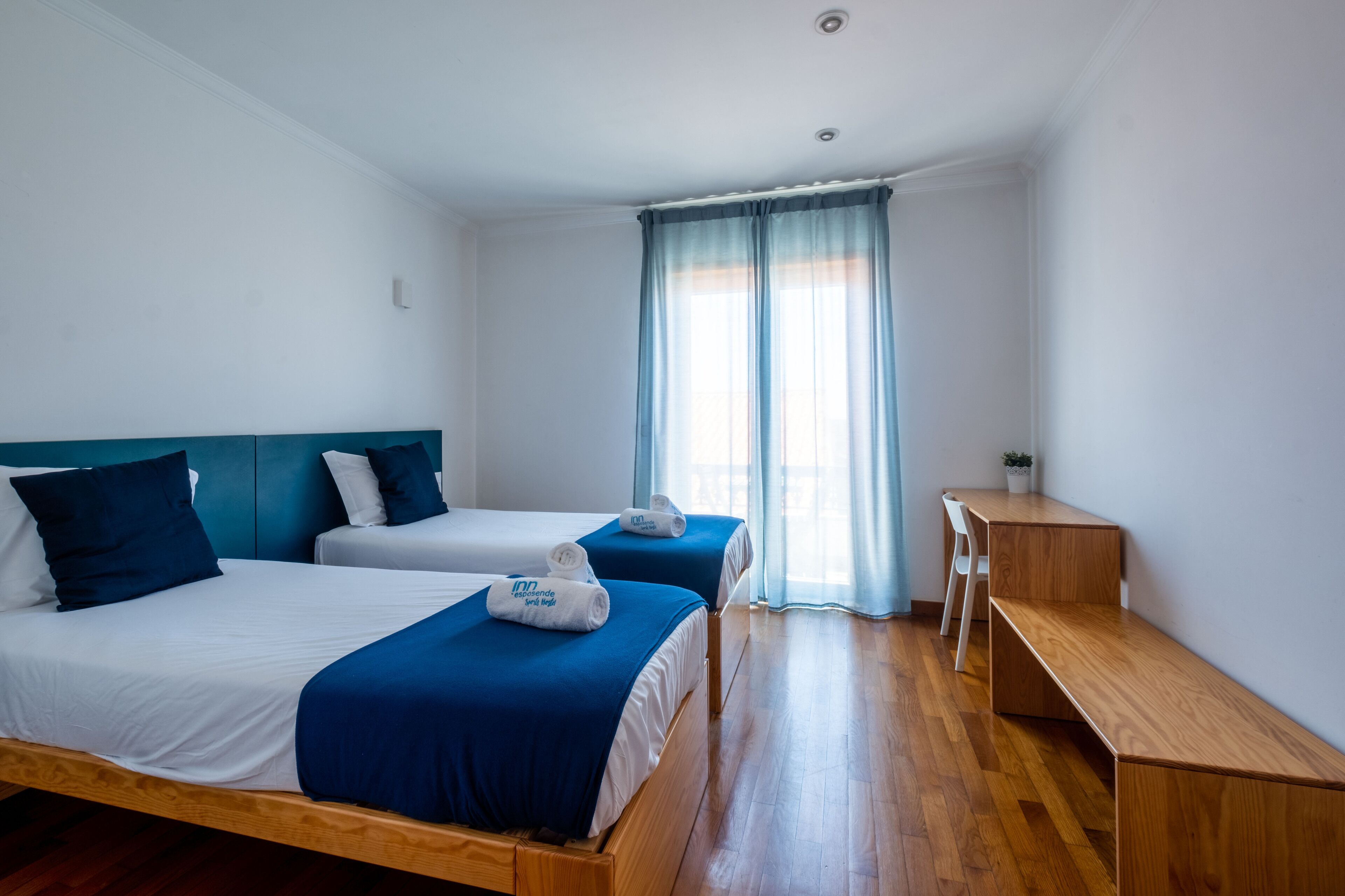 Ein Hotelzimmer mit zwei Einzelbetten, einem Holztisch, einem Stuhl und einem kleinen Tisch.