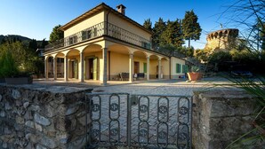 A two-story building with a balcony, arched columns, and a stone wall in the foreground. - VILLA IL TORRIONE: Elegance and luxury home between Lucca and Florence with SPA (Pescia)