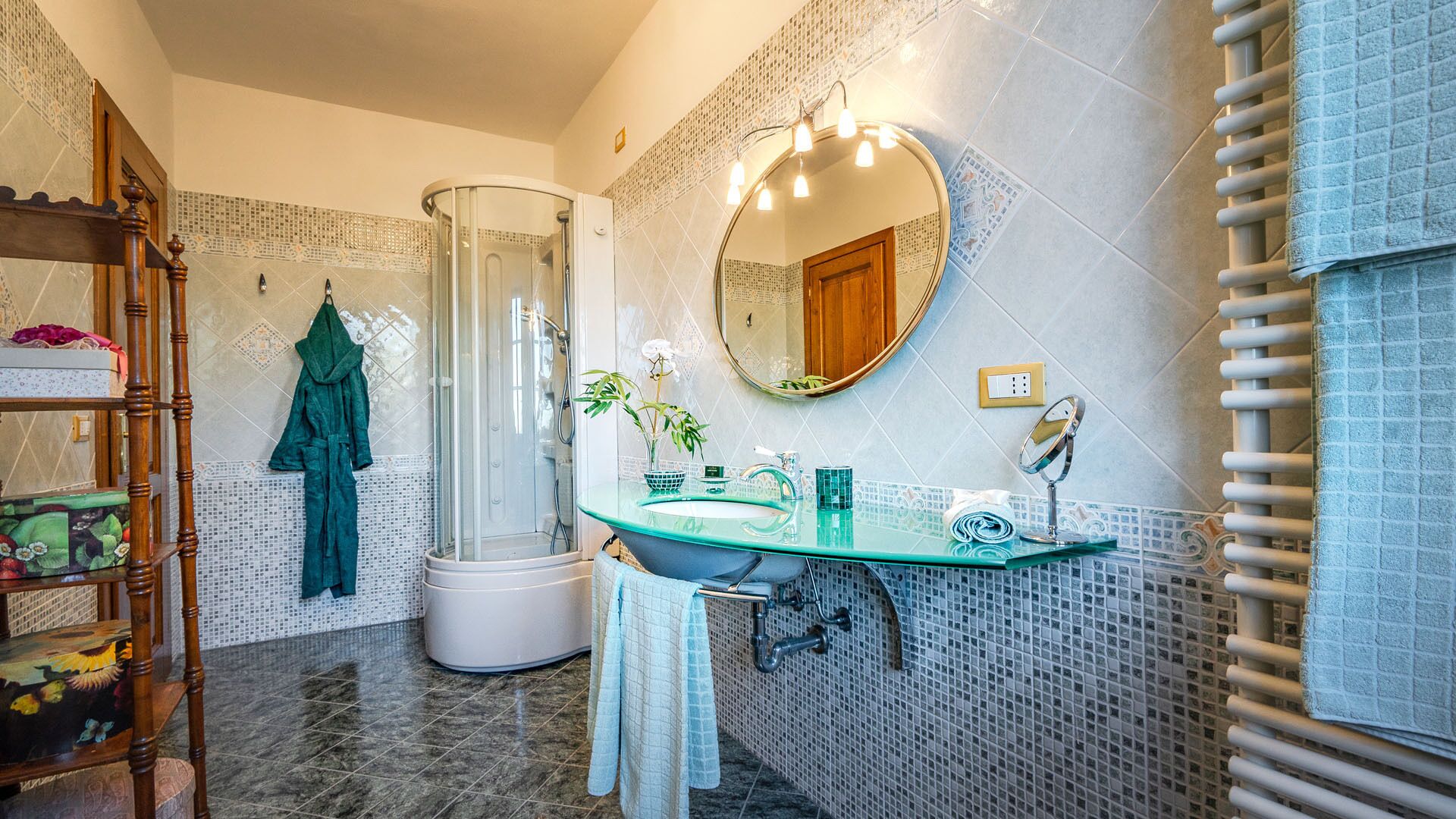 A bathroom with a glass shower enclosure, a glass sink, a wooden vanity, and a mirror.