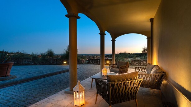 An outdoor patio with a view of the city at dusk, featuring a table and chairs, a lantern, and a potted plant. - VILLA IL TORRIONE: Elegance and luxury home between Lucca and Florence with SPA (Pescia)
