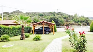 A garden with a paved path, a wooden gazebo, and a black car parked nearby. - Monad Villa Hellas Hanioti (Kassandra)