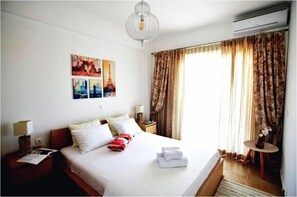 A hotel room with a large bed, two bedside tables, a chandelier, and a window with curtains. - Monad Villa Hellas Hanioti (Kassandra)