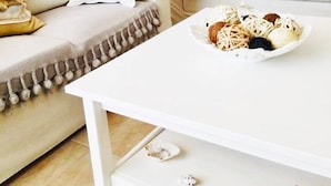 A living room with a white sofa, a white coffee table with decorative items, and a kitchen in the background. - Monad Villa Hellas Hanioti (Kassandra)