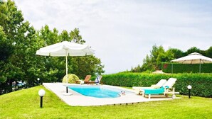 A swimming pool with lounge chairs and umbrellas, surrounded by well-maintained grass and hedges. - Monad Villa Hellas Hanioti (Kassandra)